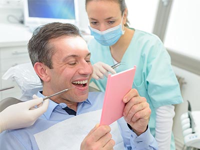 The image shows a dental professional holding up an open pink envelope with a surprised expression while sitting at a dental chair.