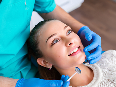 A woman receiving dental care with a smile, assisted by a dentist wearing gloves and a mask.